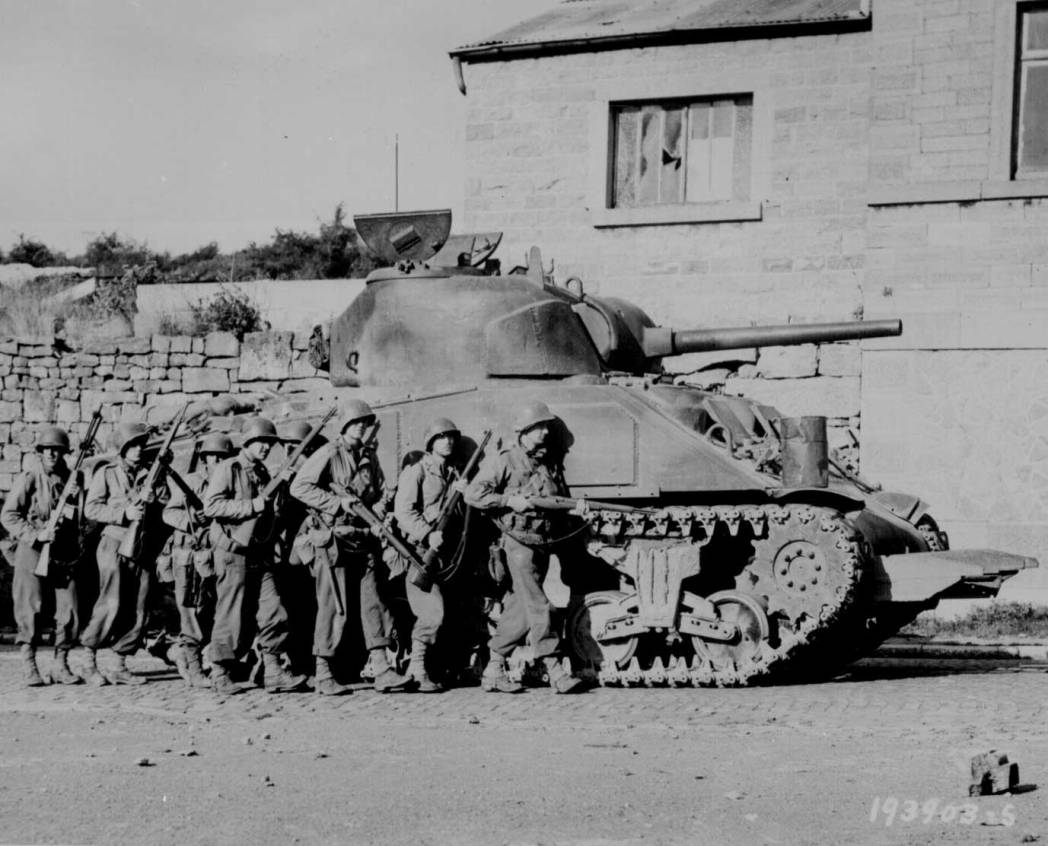 Infantry men advance under the cover of a M4 Sherman tank in Sprimont, Belgium, 9th September 1944.