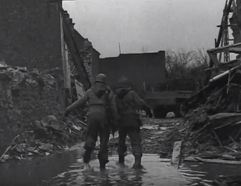 2 American GIs walk towards the truck to pick up the prisoners.